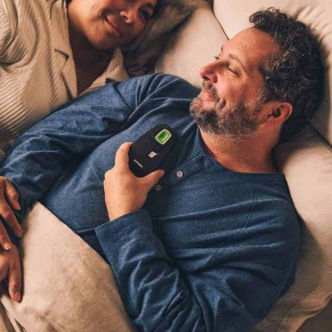 A couple lying in bed and smiling while the man holds an Inspire machine